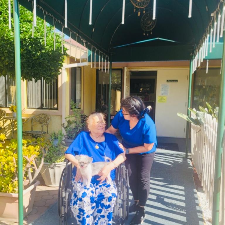 Resident in wheelchair with staff and dog at entrance.