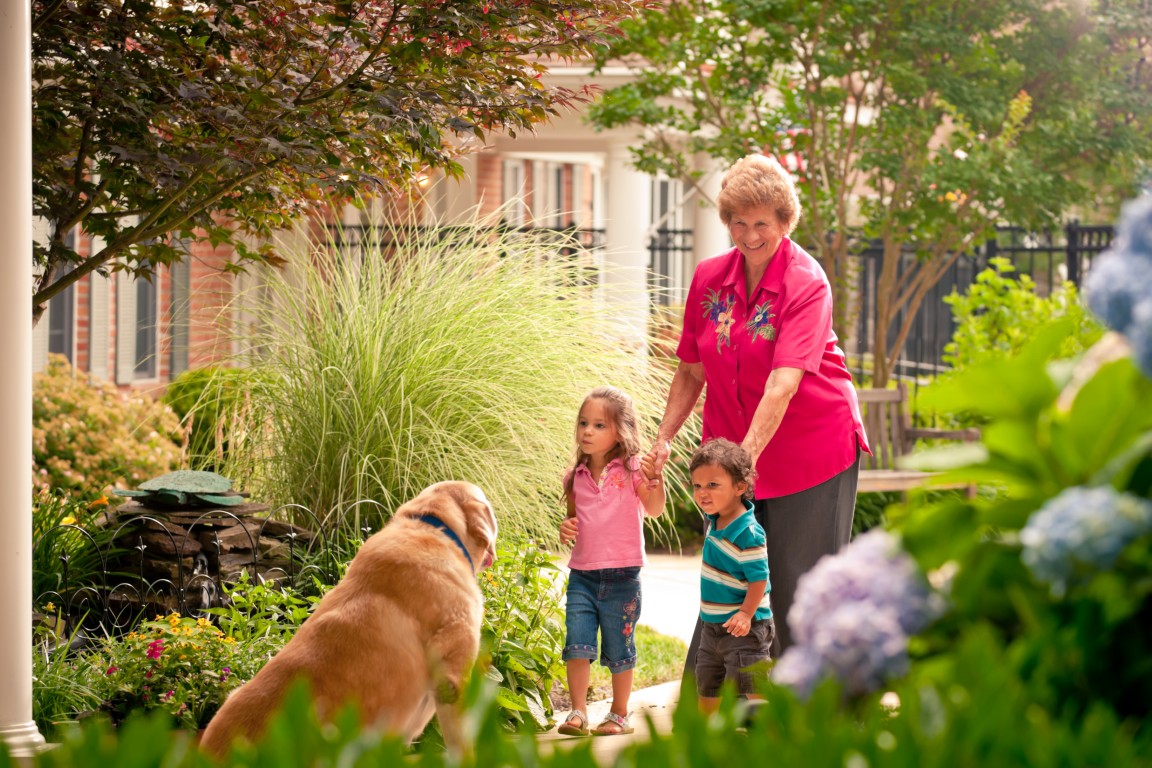 An elderly woman interacting with children and a dog in a garden