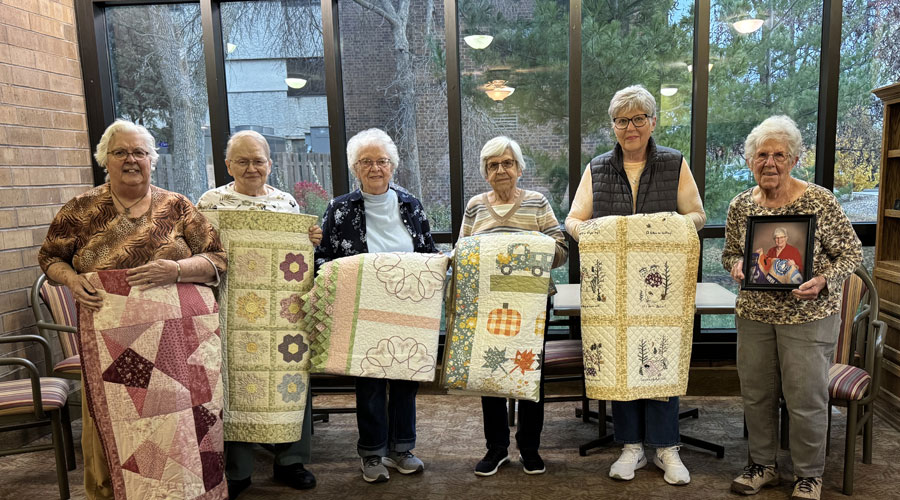 Residents showcasing handmade quilts in a common area