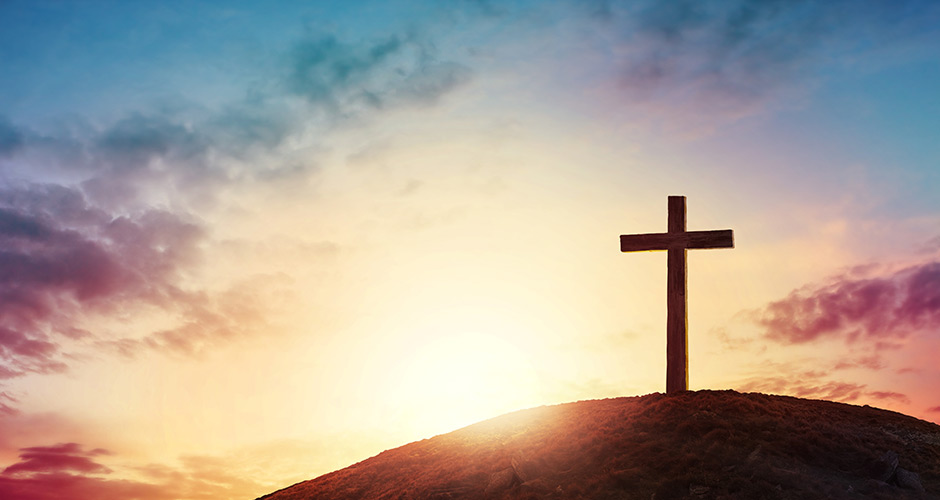 Silhouette of a cross on a hill during sunset
