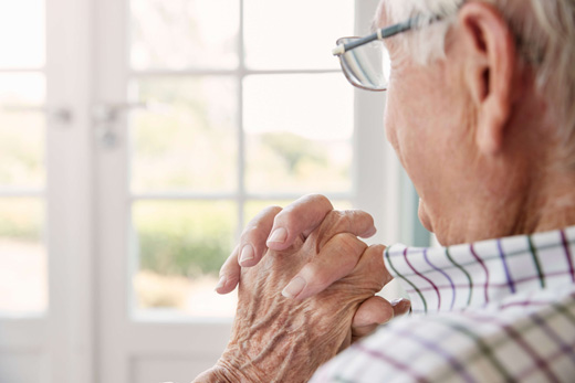 An elderly man with clasped hands, gazing out a window
