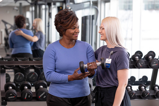 Staff assisting a resident with weights in a fitness area
