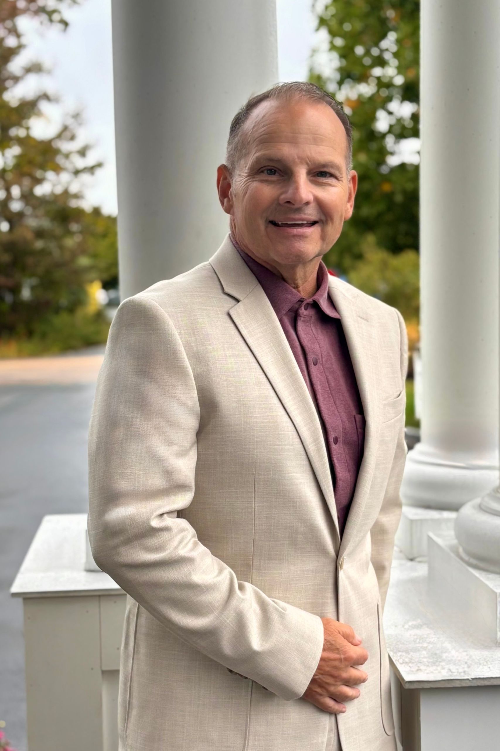 A man in a blazer standing outdoors smiling