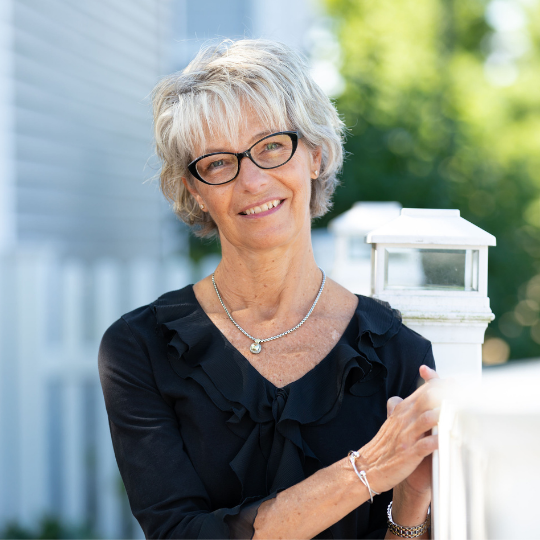 A smiling woman poses outdoors near a white fence