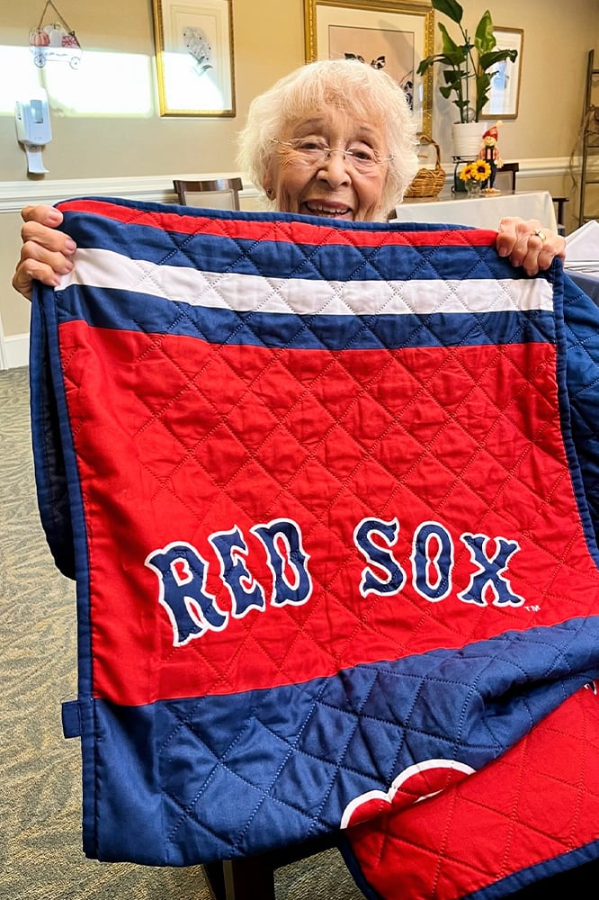 Elderly woman holding a Red Sox blanket in a common area
