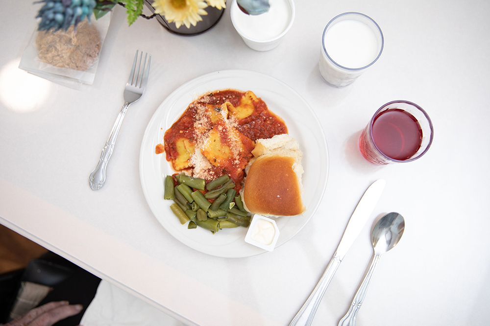 A plate of food with green beans, ravioli, and a roll
