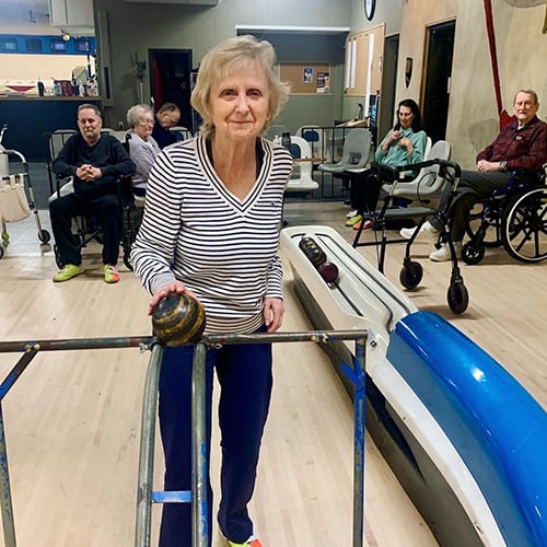 Resident participating in a bowling activity with others in the background