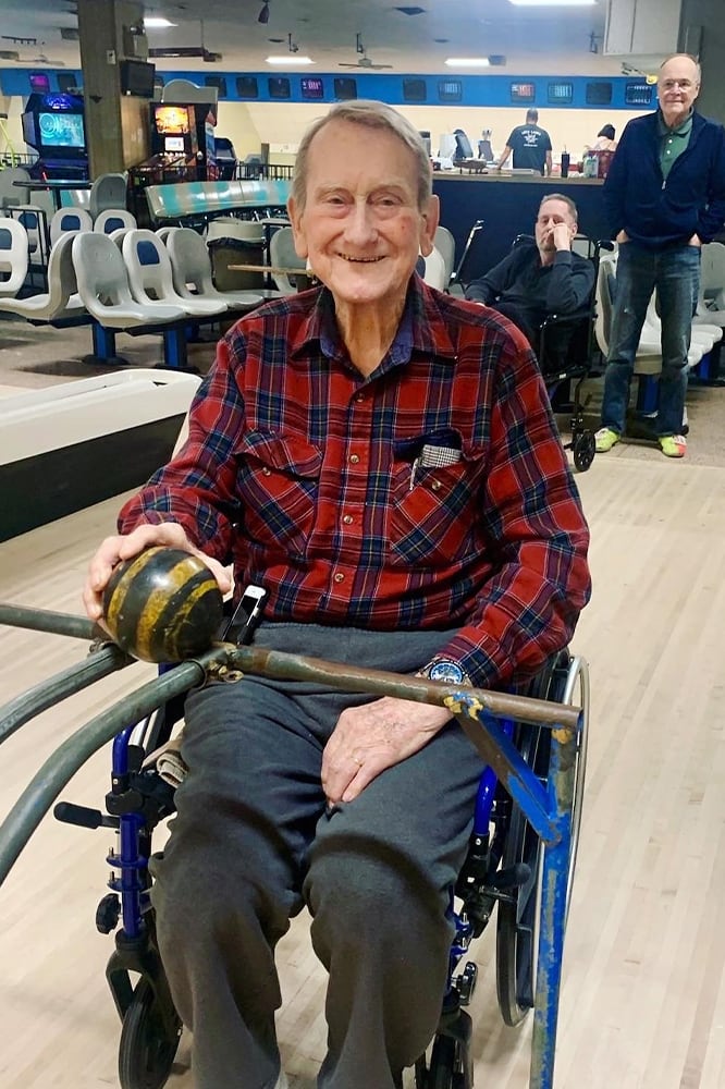 Senior resident bowling with assistance in a cheerful setting