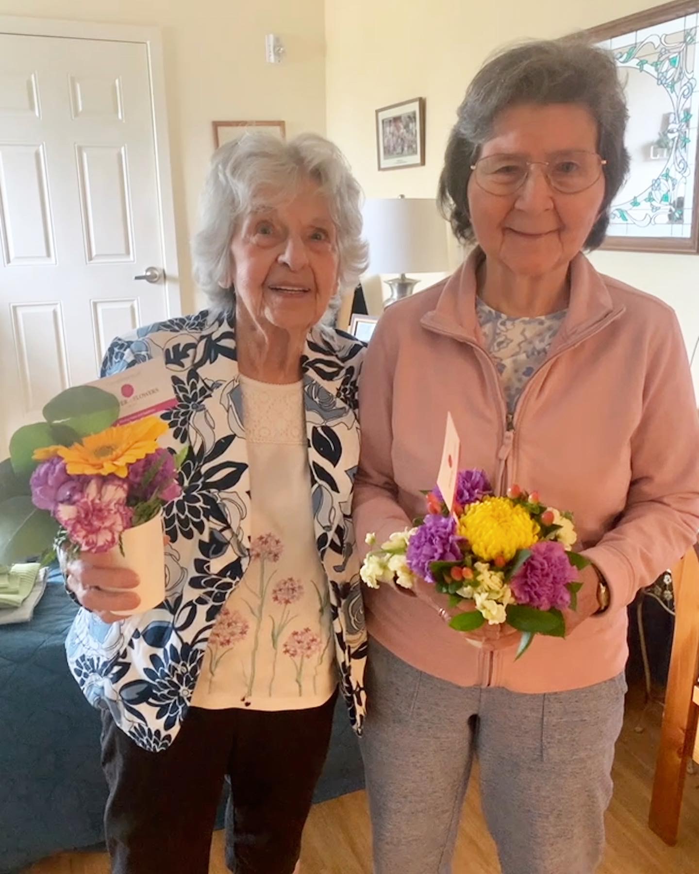 Two residents holding flower arrangements inside the facility