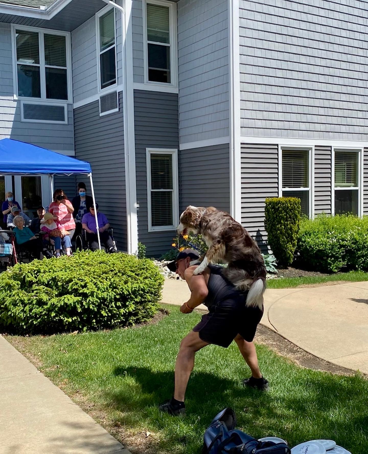 Man playfully lifting a dog, with residents watching.