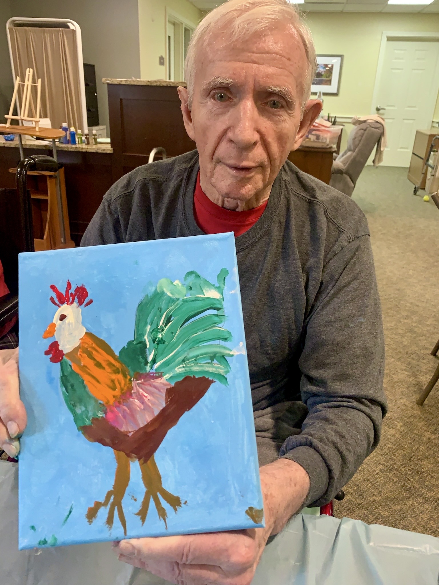 An elderly man displaying his colorful painting of a rooster