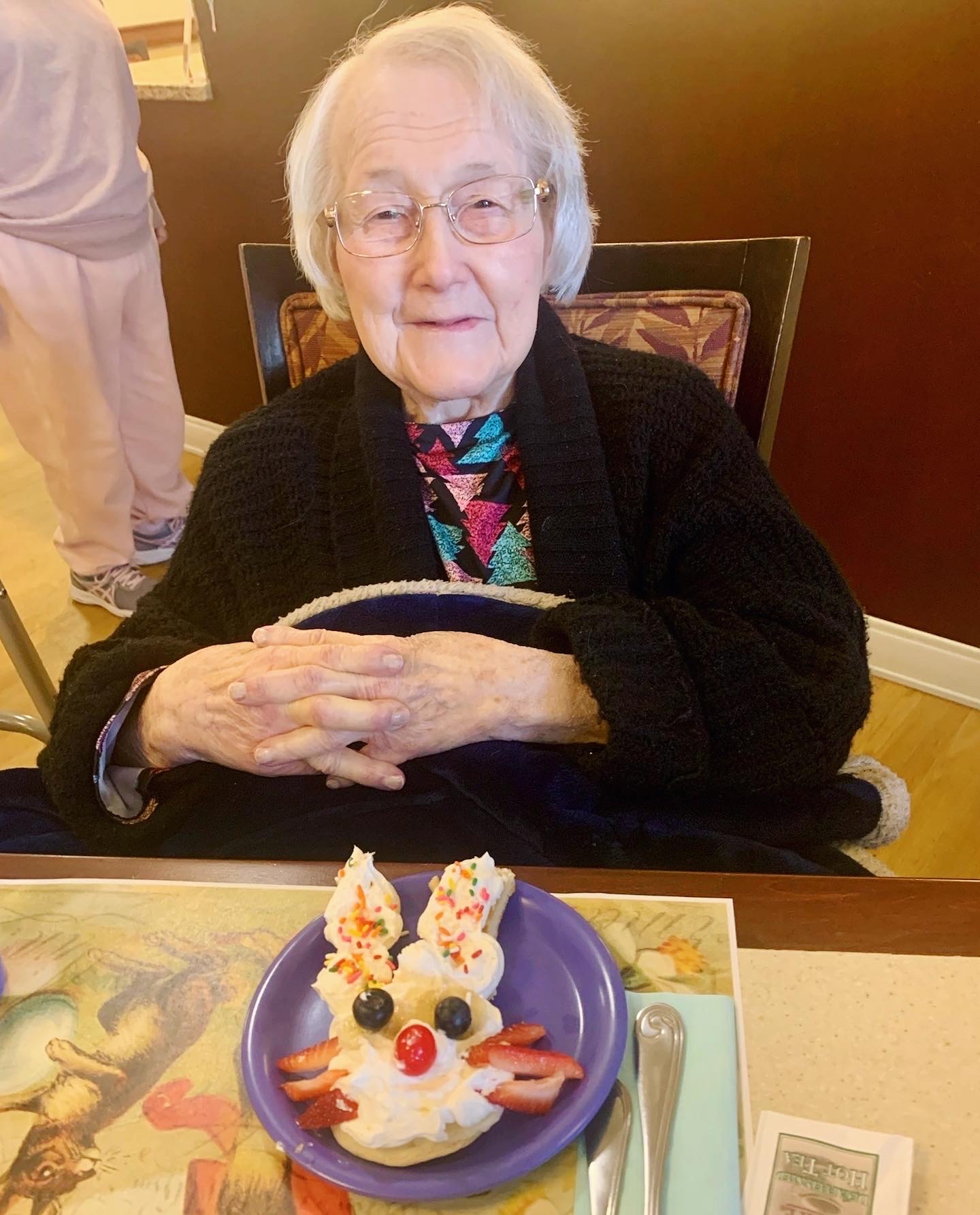 An elderly woman smiles with a dessert shaped like a bunny
