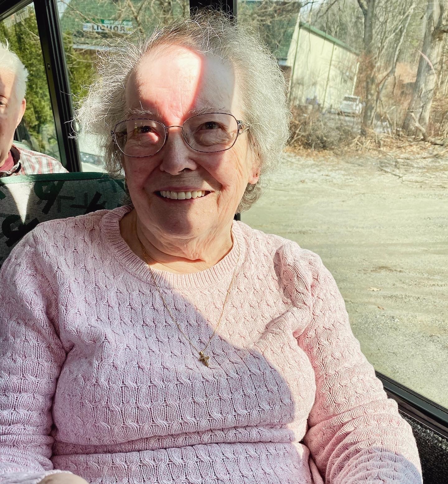 A smiling resident in a pink sweater inside a transport vehicle
