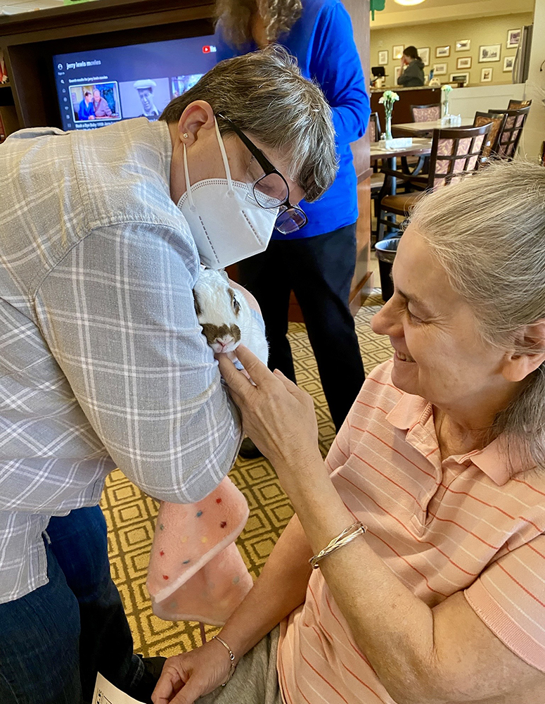 Resident interacting with staff and a small pet in a common area