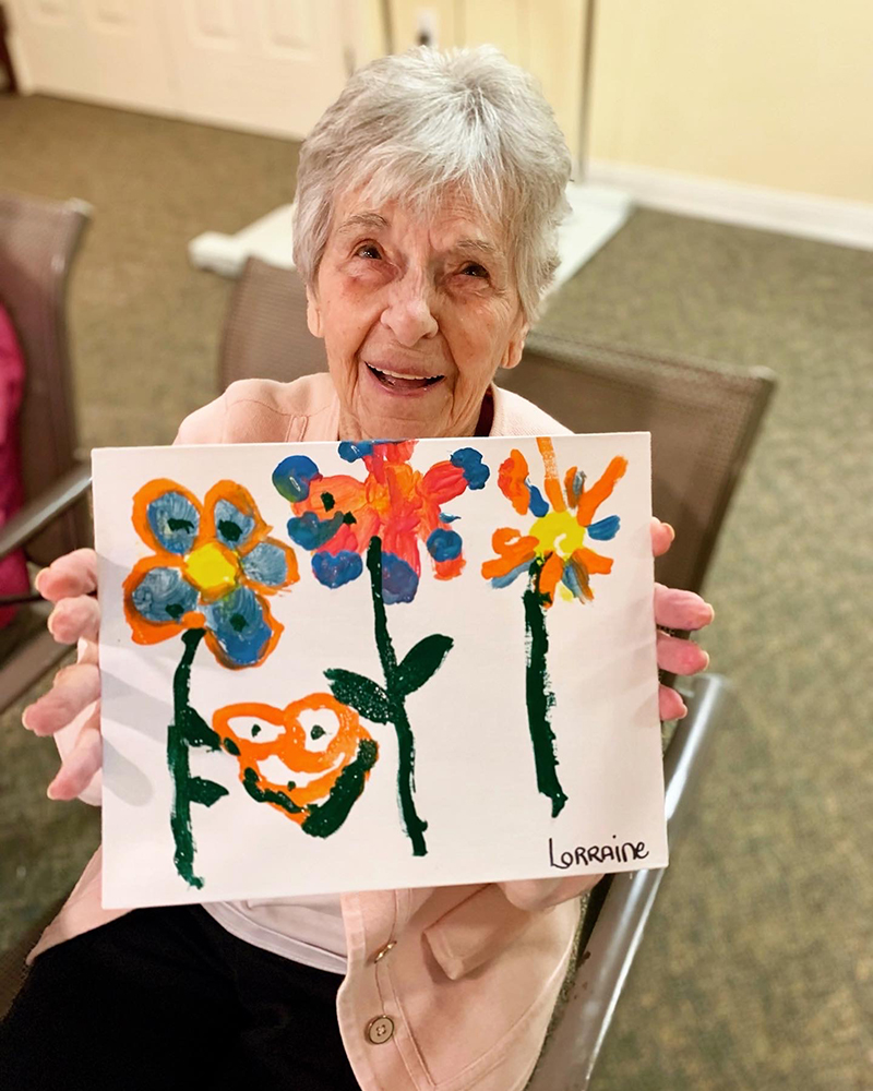 Resident holding a colorful painting in an activity room