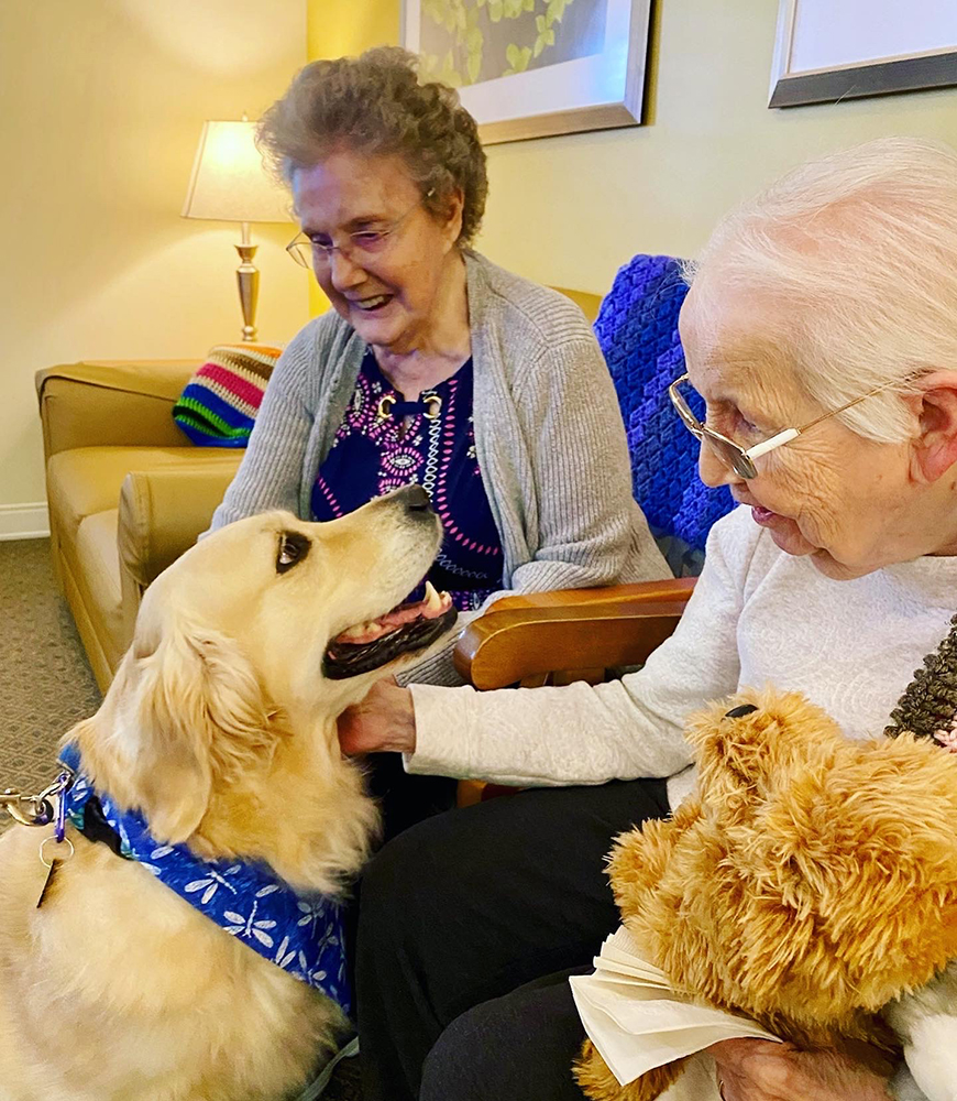 Two residents enjoying time with a dog in a cozy lounge
