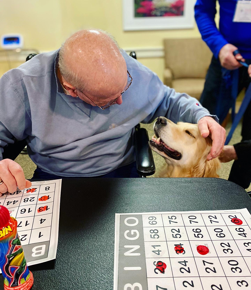 Resident playing bingo with a pet therapy dog