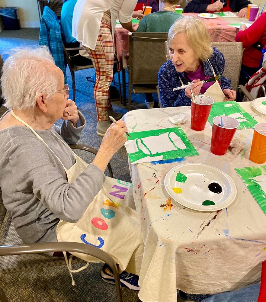 Two residents painting together in an activity room