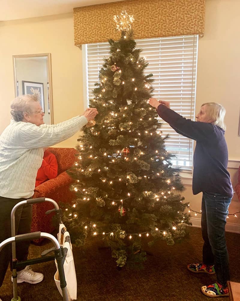 Residents decorating a Christmas tree in a common area