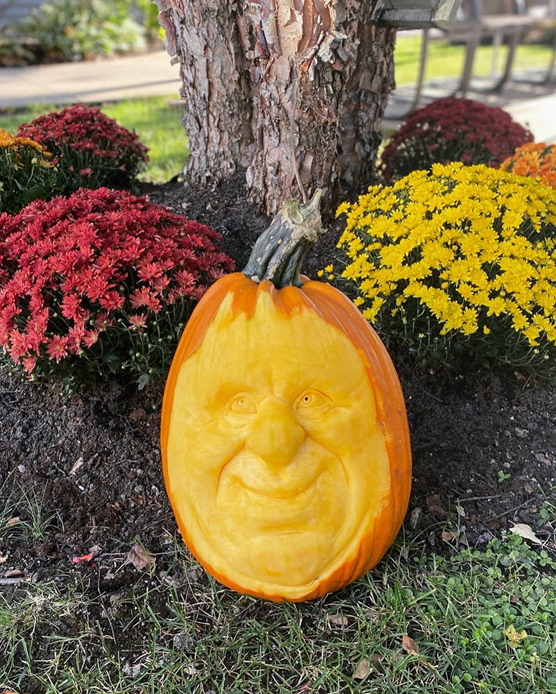 A carved pumpkin face amidst colorful flowers