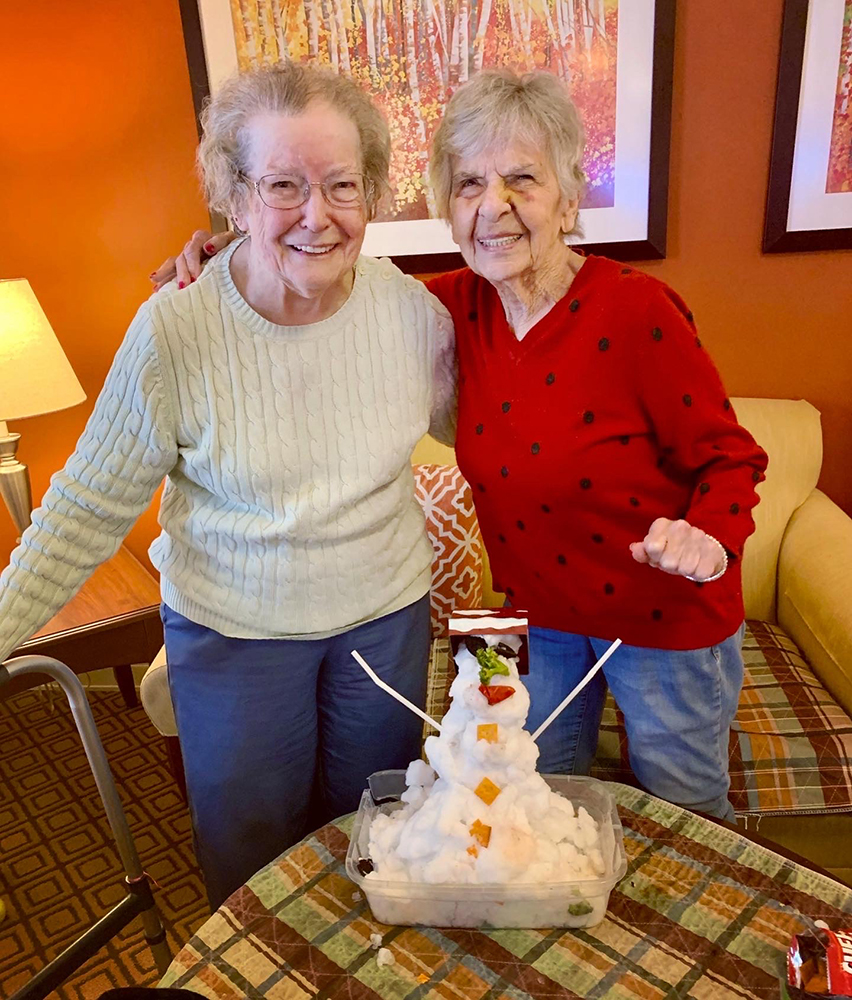 Two residents celebrating with a snowman made of snow.
