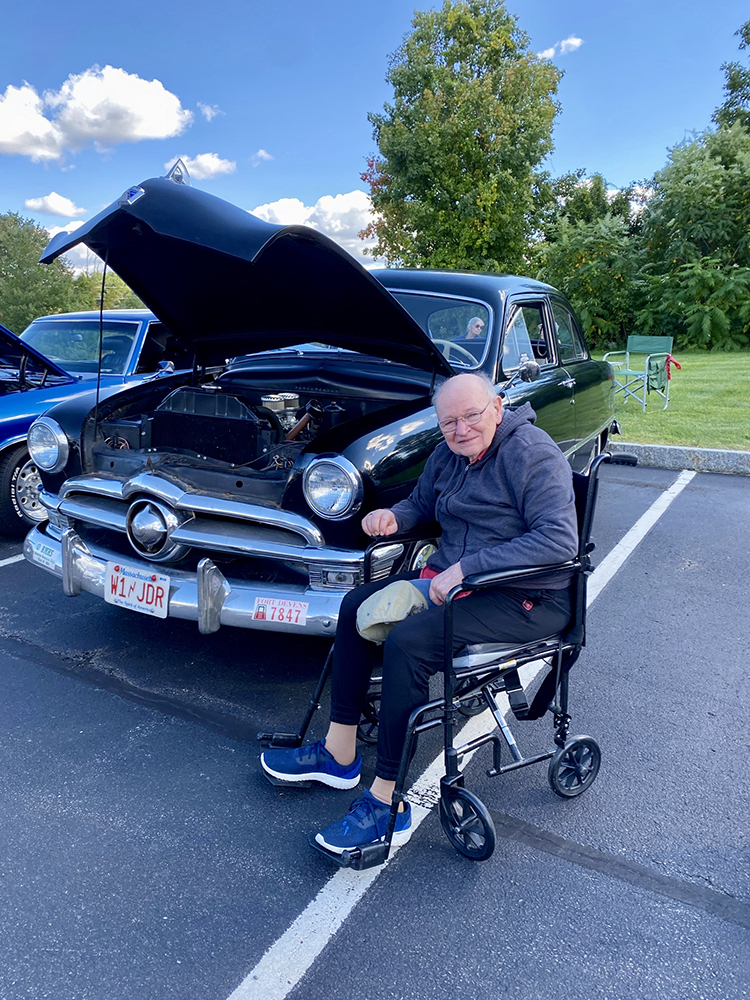 Senior resident posing with a classic car in a parking lot