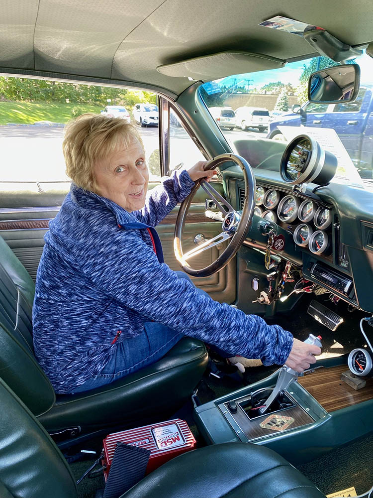 A woman inside a classic car, smiling.