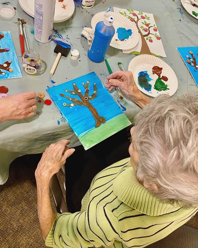 A resident painting a tree during an art activity