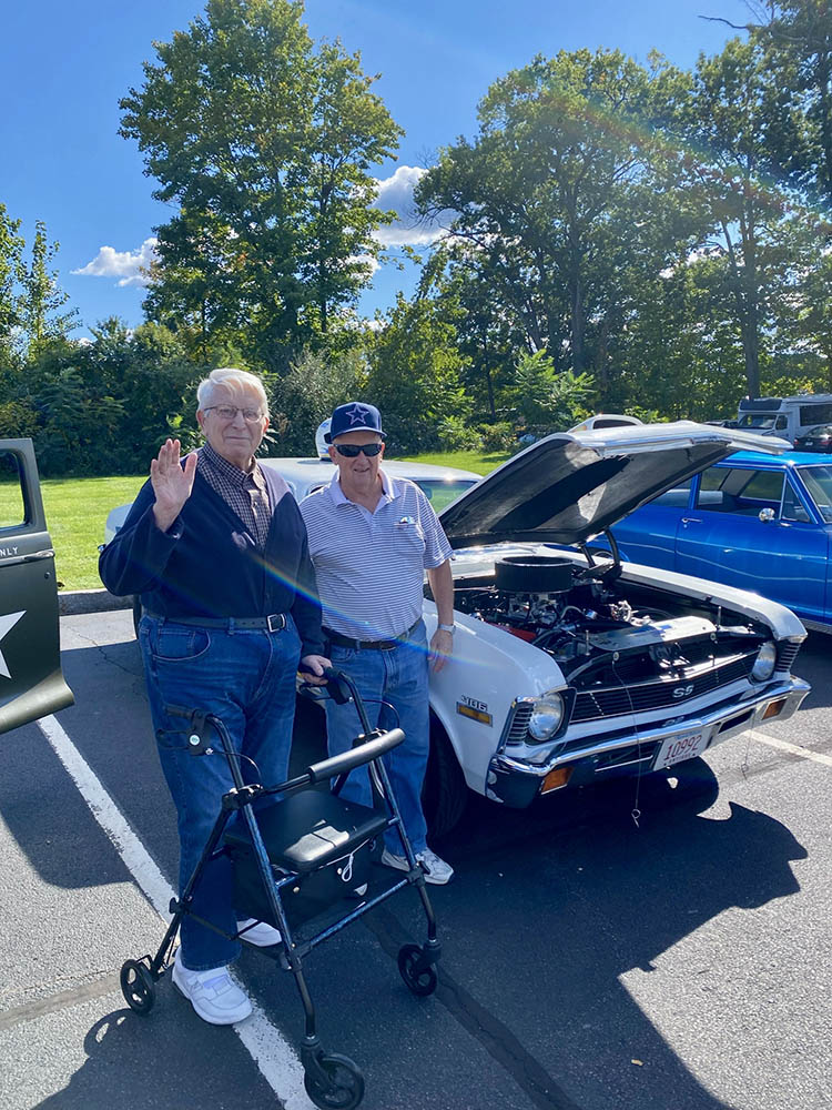 Two seniors socializing next to a classic car outdoors