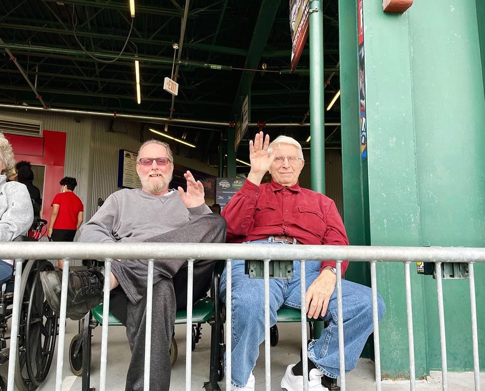 Two residents waving while seated outdoors