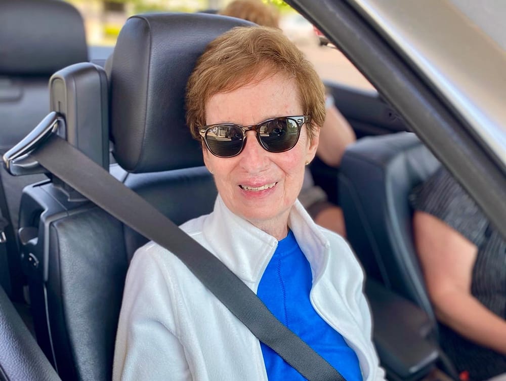 A smiling woman in sunglasses seated in a vehicle