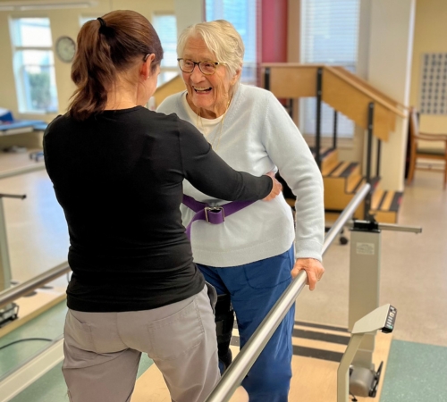 A staff member assisting a senior resident with mobility exercise