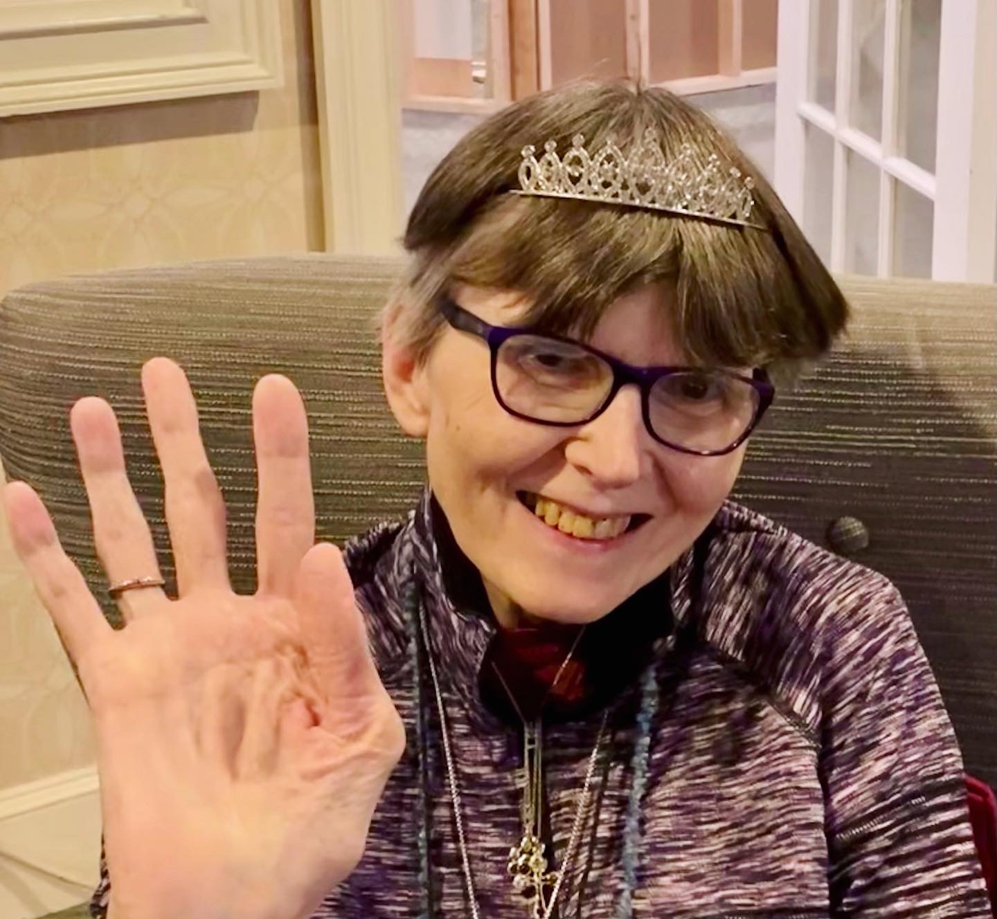 A senior resident smiling and waving with a tiara