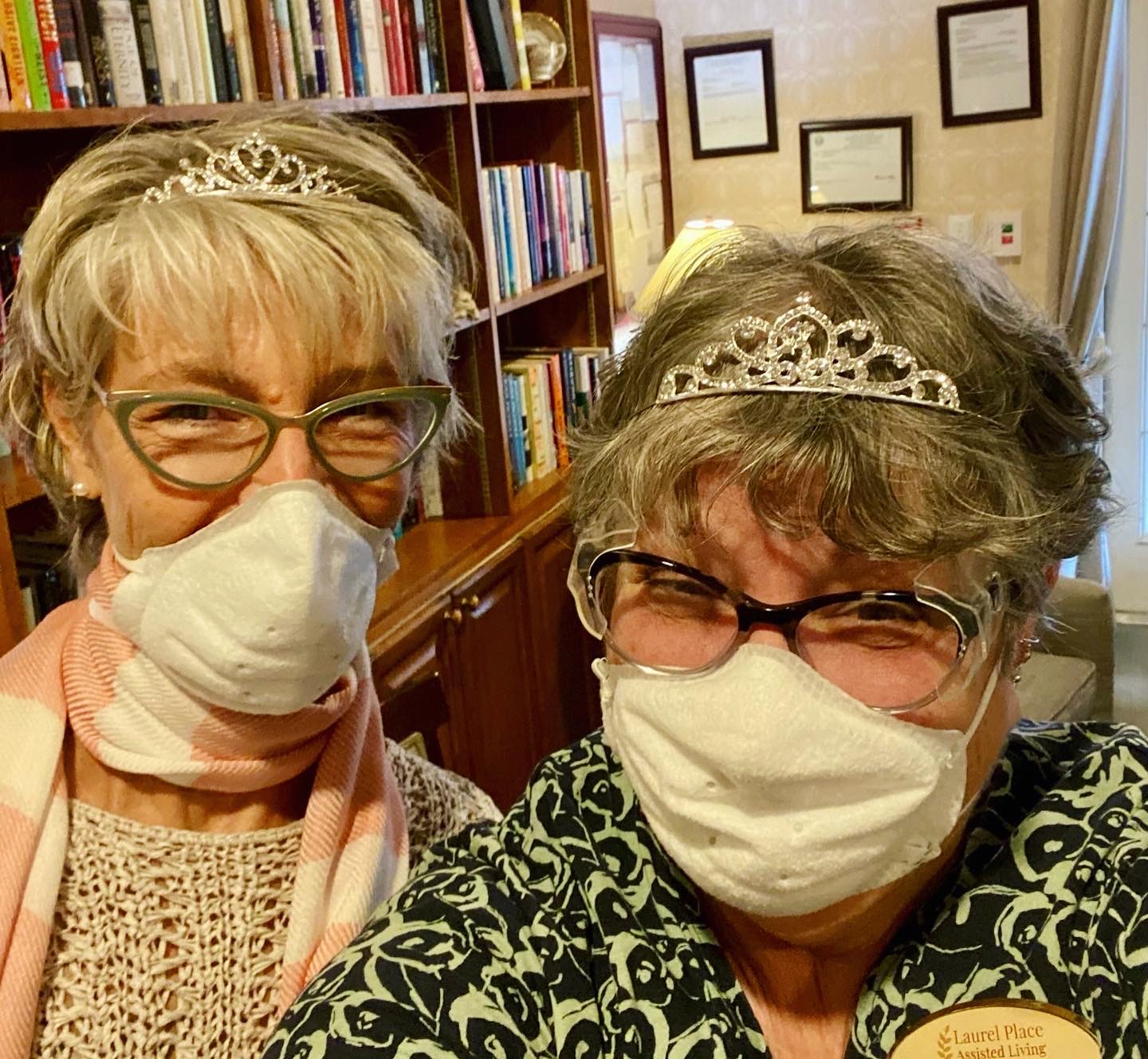 Two staff members wearing tiaras and masks in a cozy interior