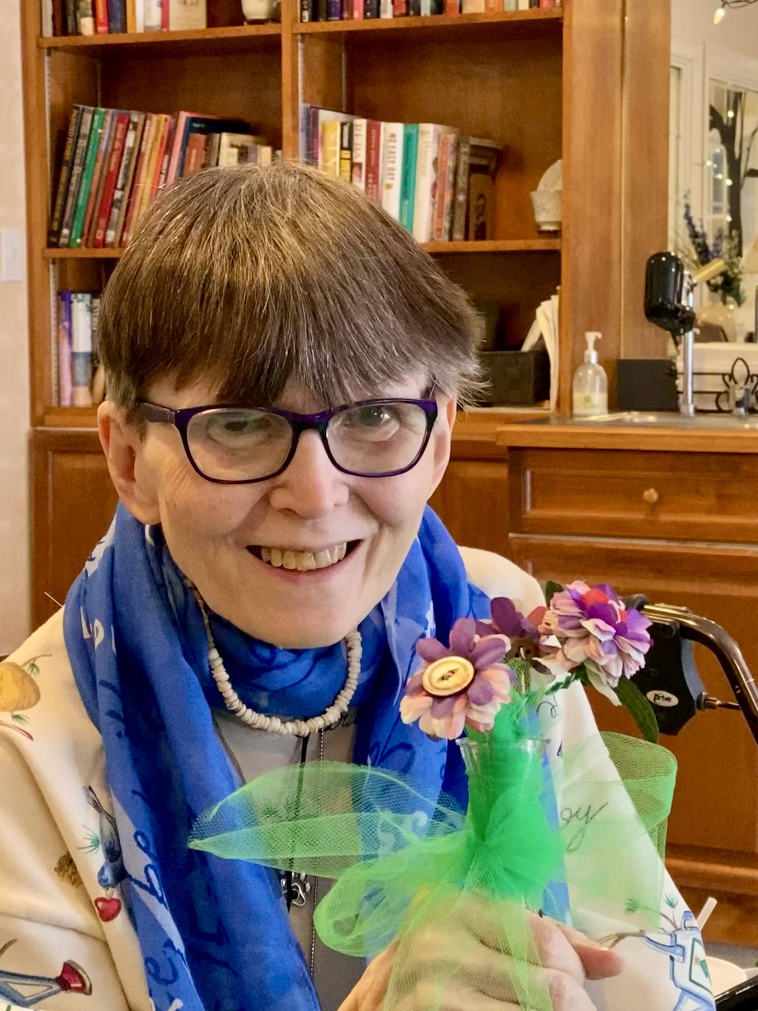 A resident smiling with flowers in a common area