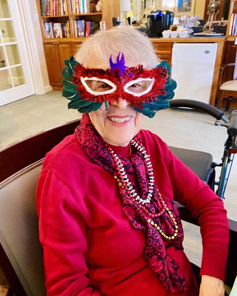 Resident wearing a colorful mask and beads in a festive interior