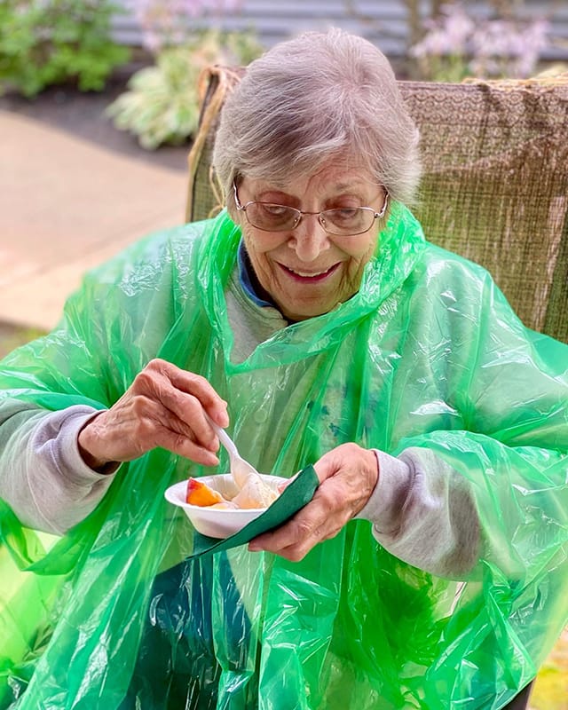 Senior resident enjoying a dessert outdoors in a rain poncho