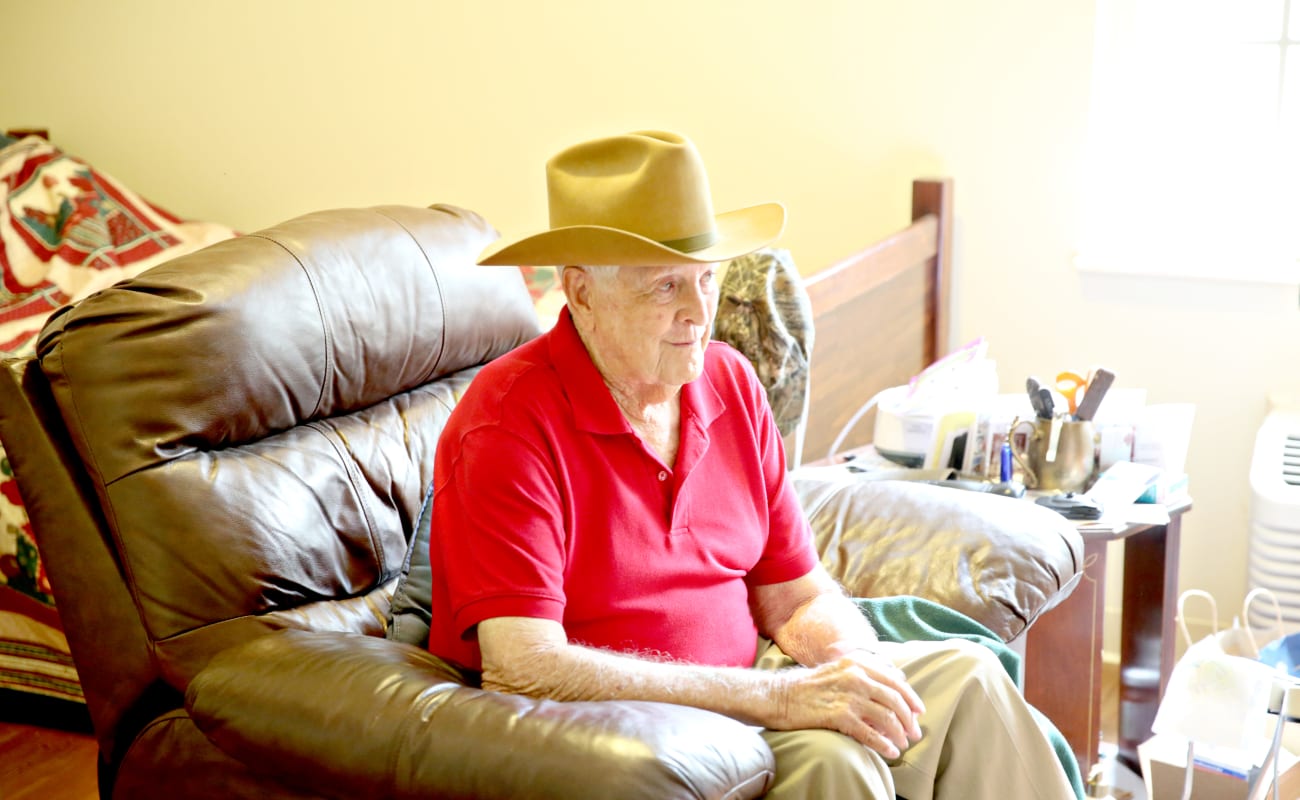 An elderly man sitting in a chair wearing a cowboy hat