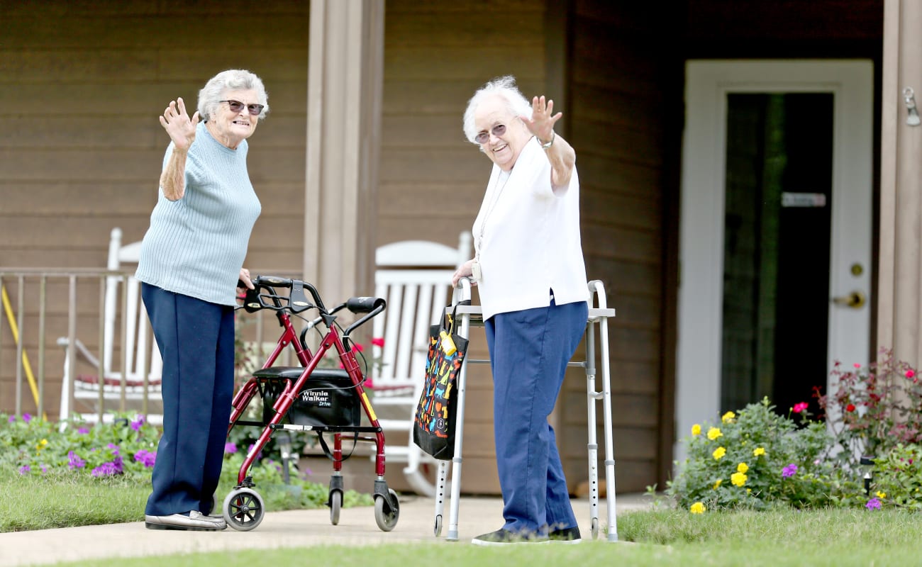 Two residents waving outside with walkers