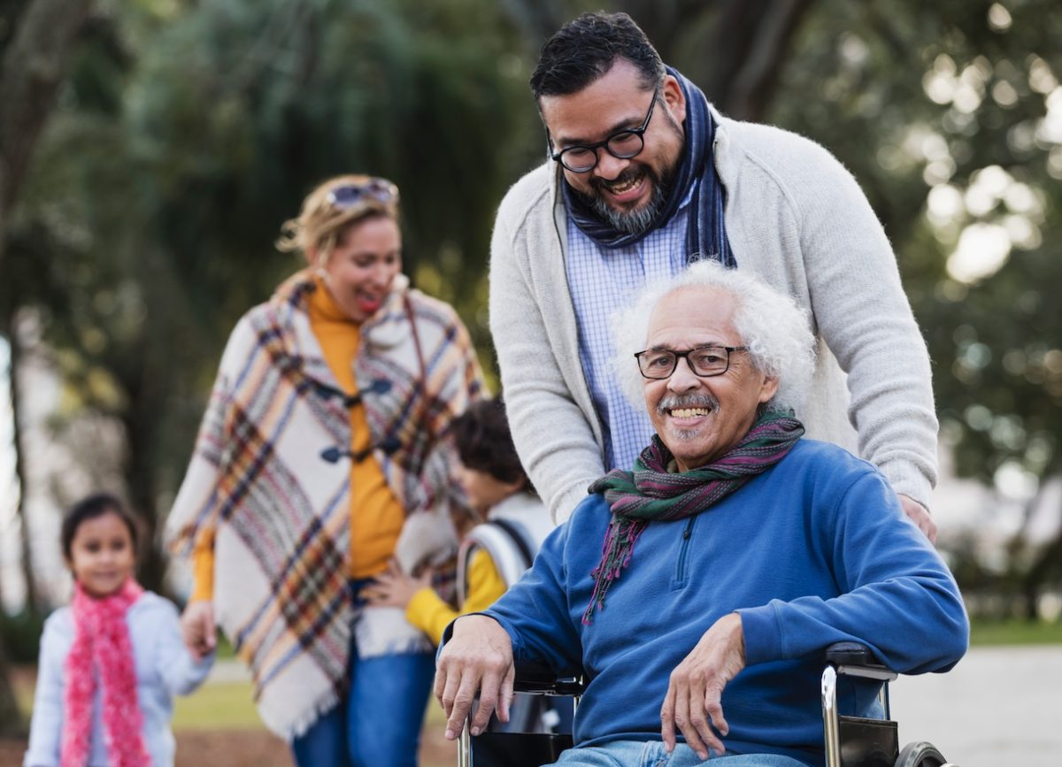A smiling elderly man in a wheelchair with family in an outdoor setting