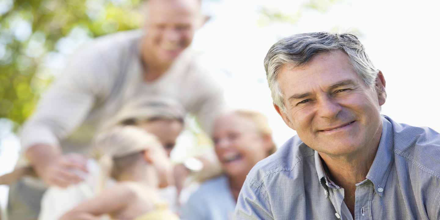 A man smiling outdoors with family behind him