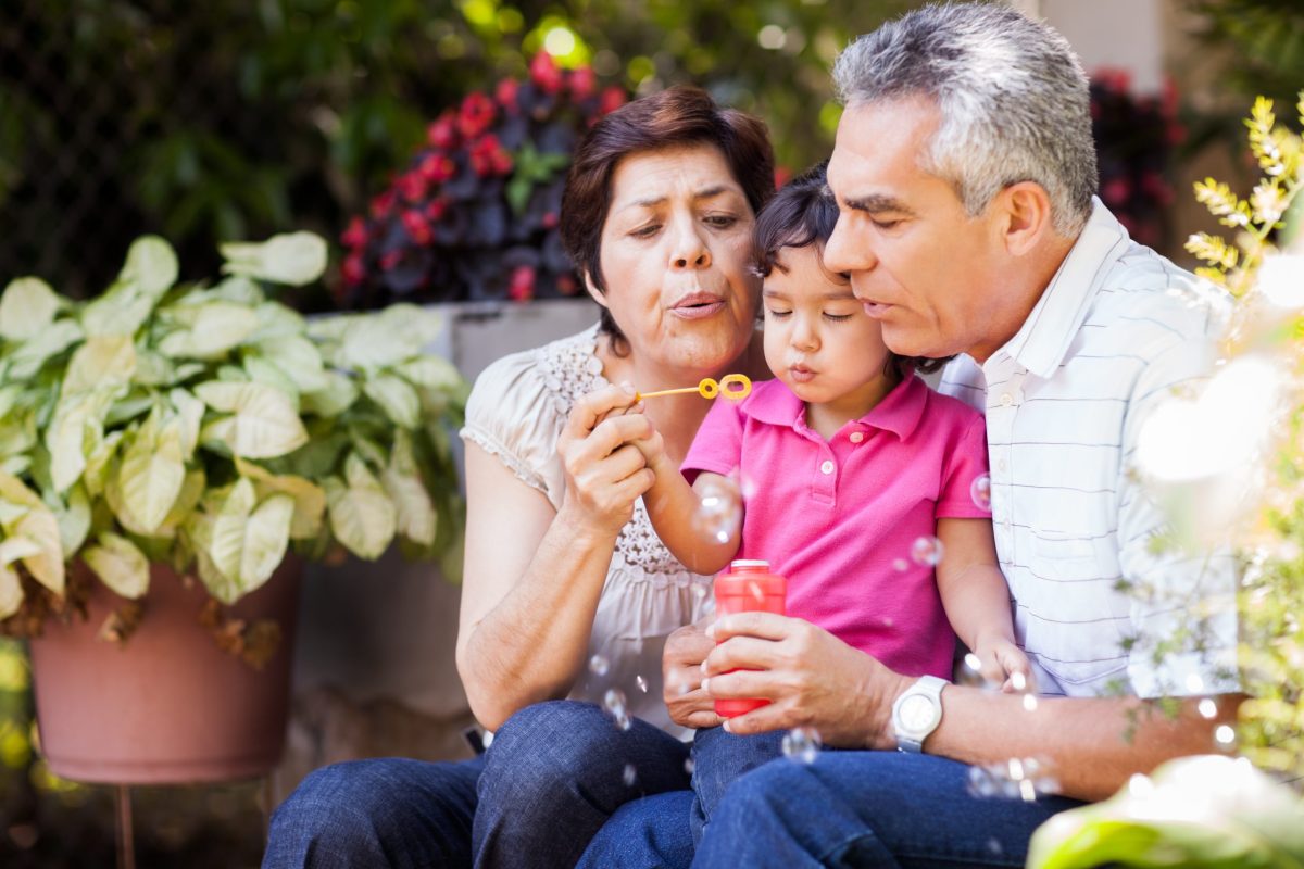 An elderly couple and a child blowing bubbles in a garden