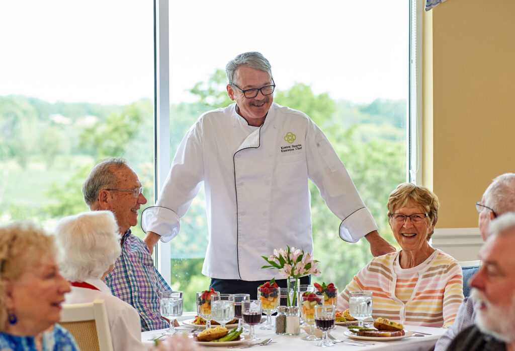 Residents enjoying a meal with a chef in a dining room