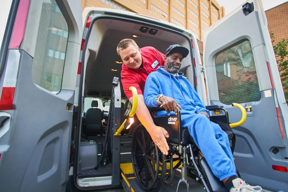 A staff member assisting a resident in a wheelchair van