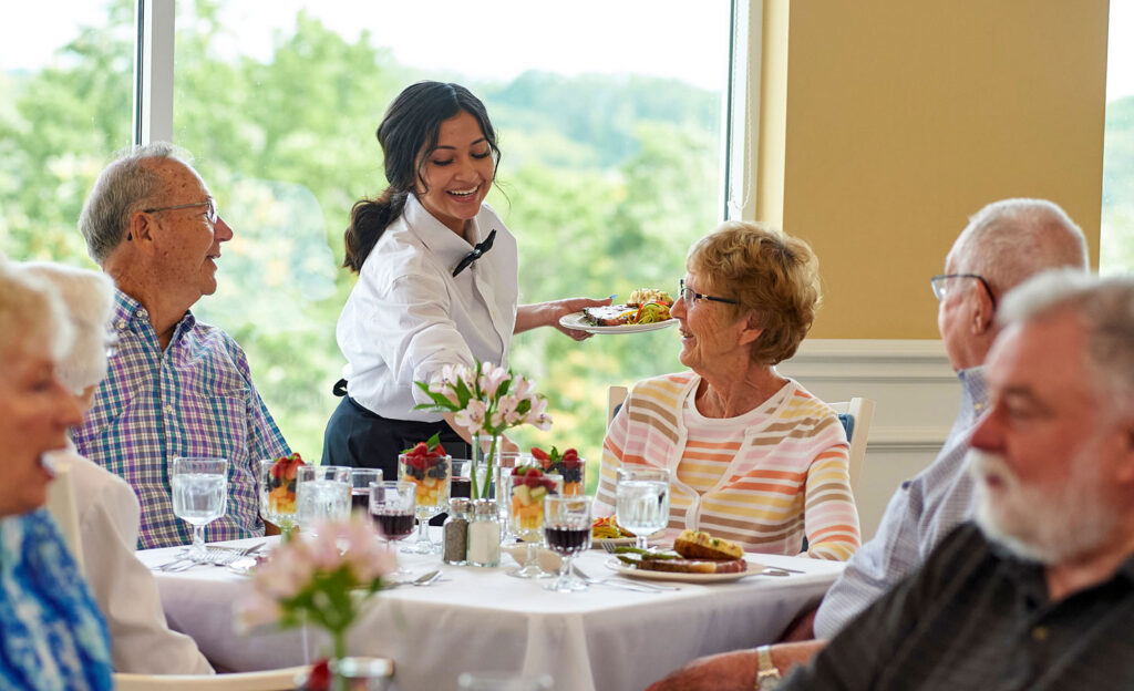 Residents enjoying a meal with attentive staff in a dining room