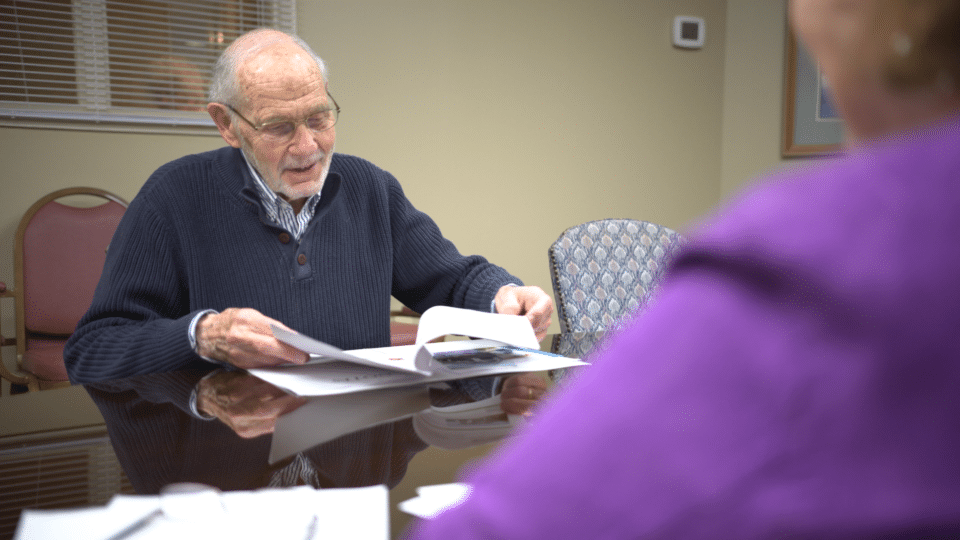 An elderly man reading documents with a visitor