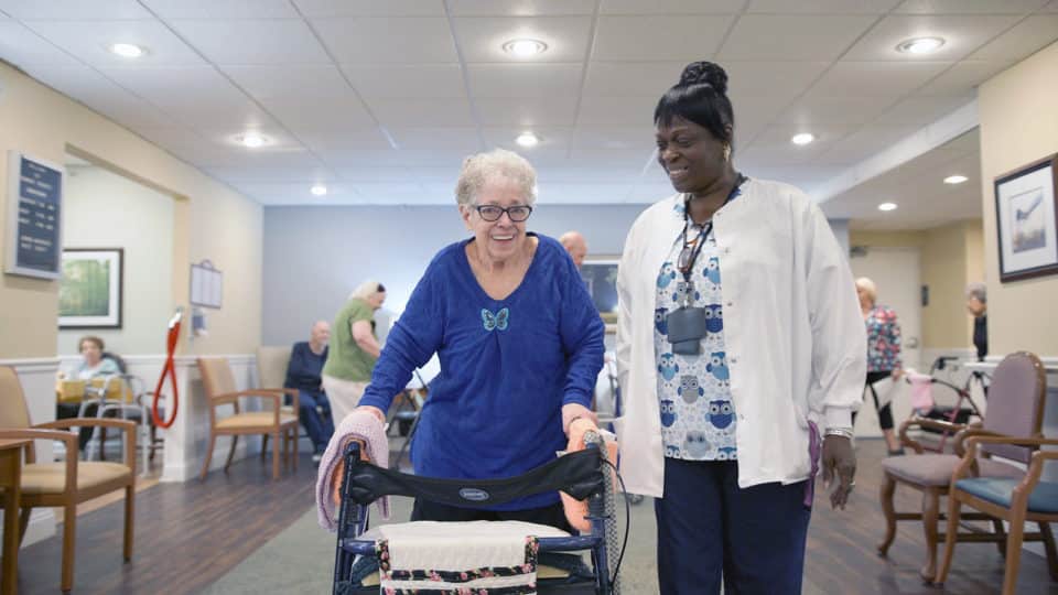 Resident using a walker with staff assistance in an activity area