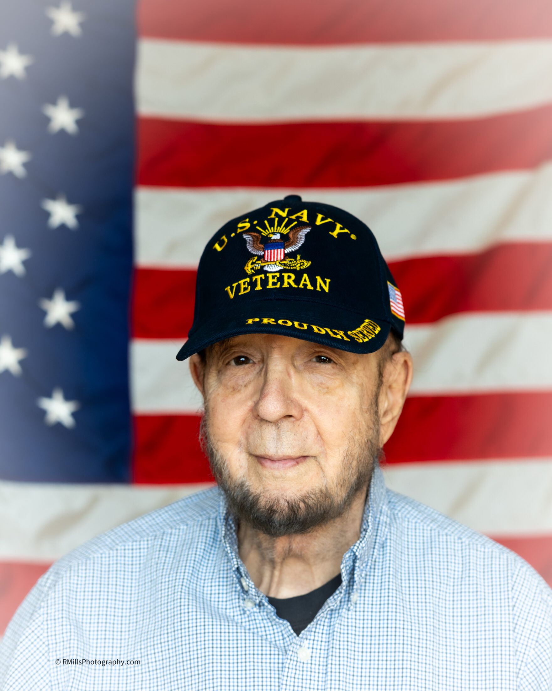 Senior veteran wearing a U.S. Navy hat in front of a flag