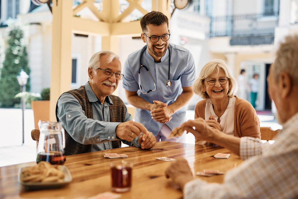 Seniors playing cards with a caregiver outdoors.