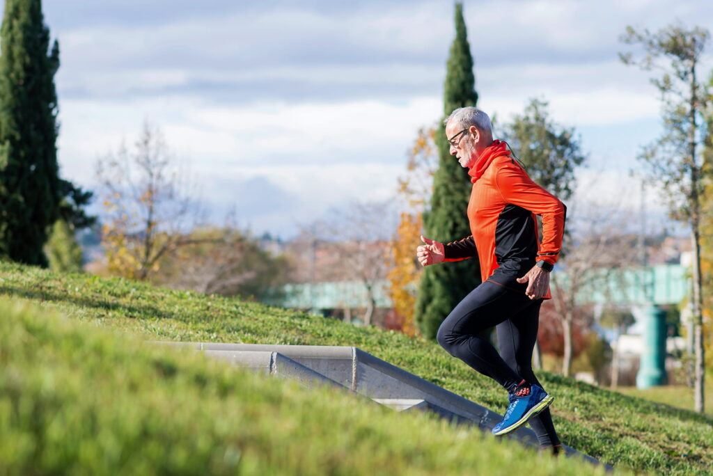 Active senior exercising outdoors on a grassy hill.